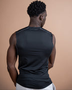A man viewed from behind wearing a black sleeveless athletic compression shirt against a solid warm beige studio background.