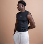 A man in a black sleeveless athletic tank top and light gray sweatpants, shown in profile against a solid warm beige background.