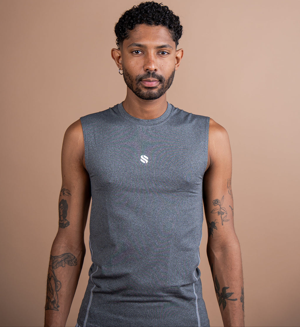A man wearing a sleeveless heather gray athletic shirt with a small white logo on the chest, standing against a solid tan background.