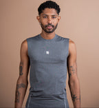 A man wearing a sleeveless heather gray athletic shirt with a small white logo on the chest, standing against a solid tan background.