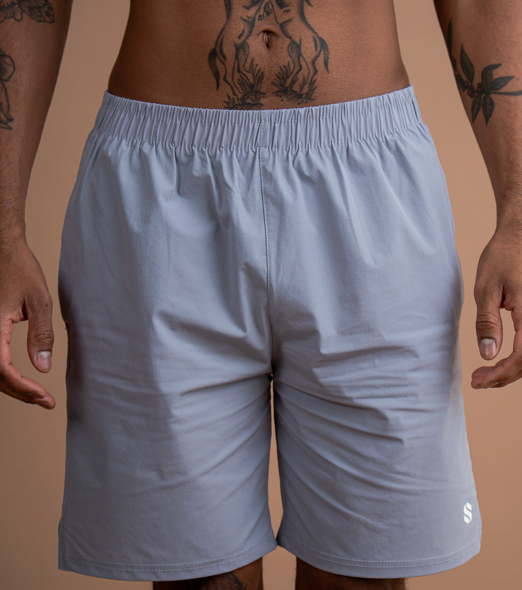 A close-up of a man wearing light gray athletic shorts, showing the waist, hips, and upper thighs. The man has visible tattoos on his torso and arms.