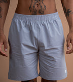 A close-up of a man wearing light gray athletic shorts, showing the waist, hips, and upper thighs. The man has visible tattoos on his torso and arms.
