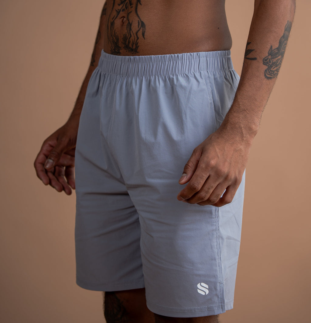 A man wearing light blue athletic shorts with an elastic waistband and a small white logo near the hem, photographed against a solid tan background.