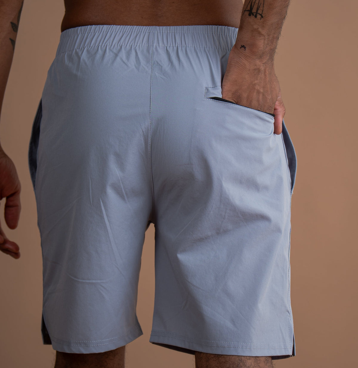 A man wearing light blue athletic shorts with dark side panels, shown from the back against a solid tan background.