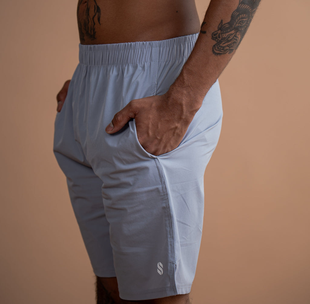 A man wearing light blue athletic shorts, shown from the chest down against a solid warm beige background.