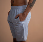 A man wearing light blue athletic shorts, shown from the chest down against a solid warm beige background.