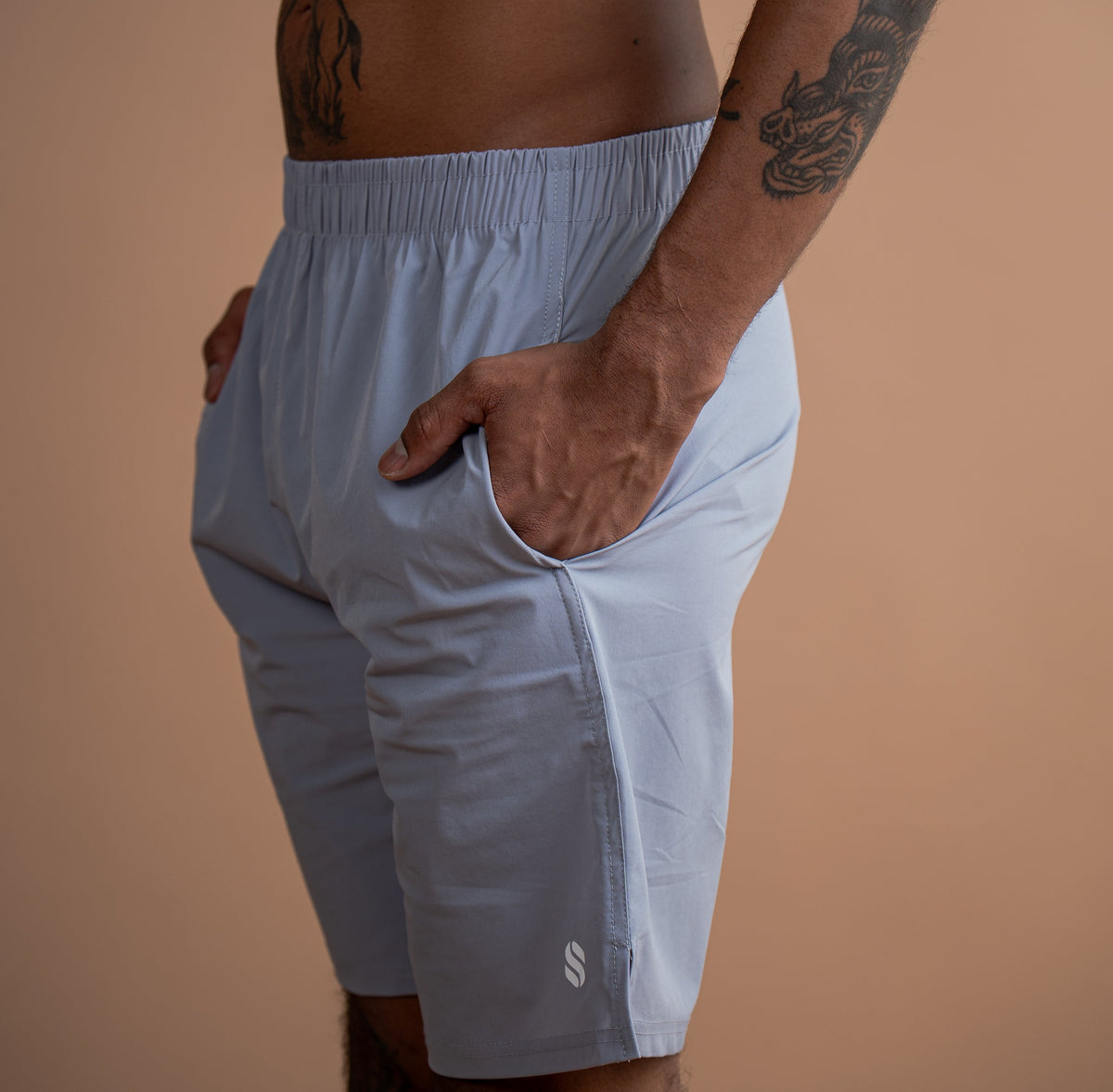 A man wearing light blue athletic shorts, shown from the chest down against a solid warm beige background.