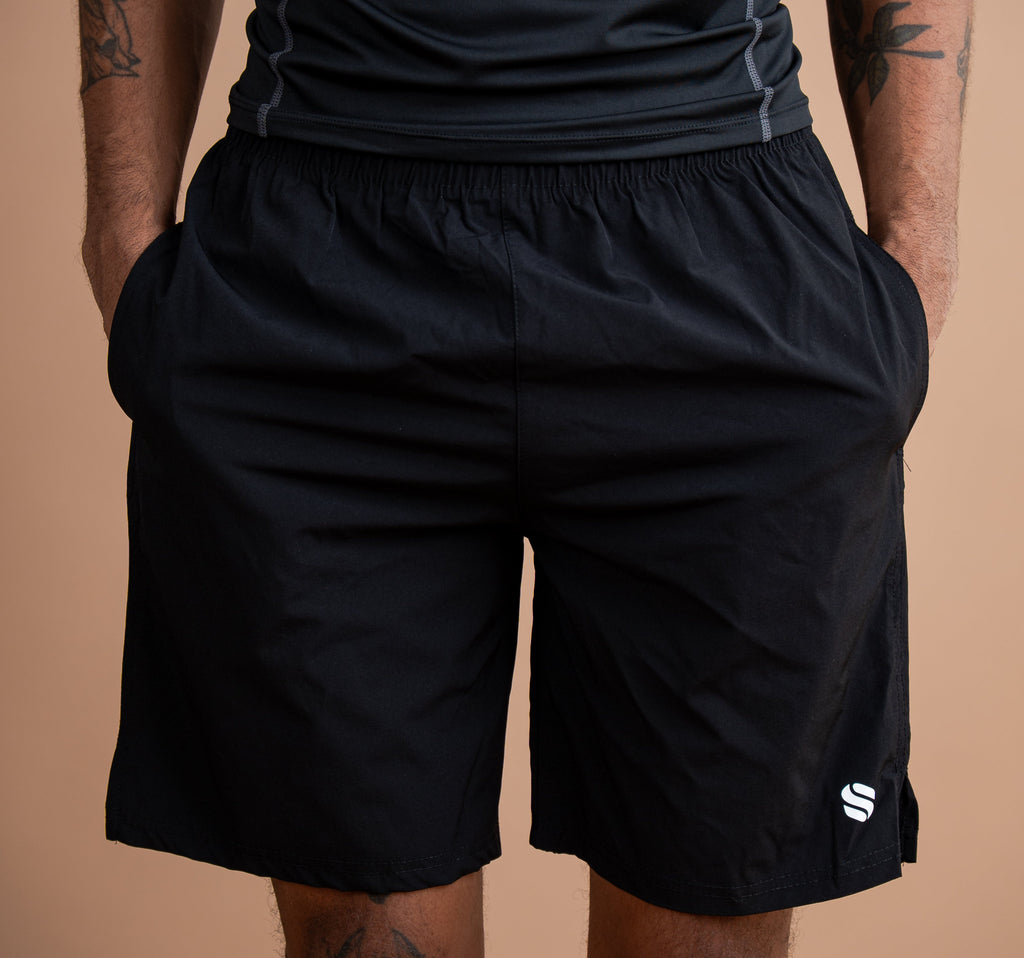 Black athletic shorts with a side logo, worn by a model against a solid tan background.