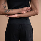 A person shown from the back wearing black athletic shorts and a black sleeveless top against a plain warm beige studio background.