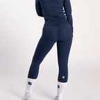 A person wears navy blue high-waisted leggings paired with a matching long-sleeved top and white crew socks with a dark logo.