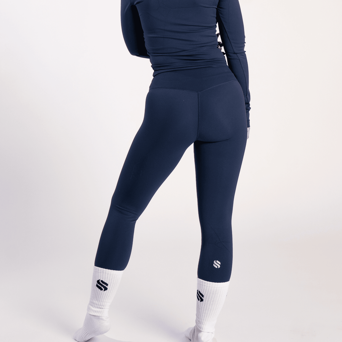 A person wears navy blue high-waisted leggings paired with a matching long-sleeved top and white crew socks with a dark logo.