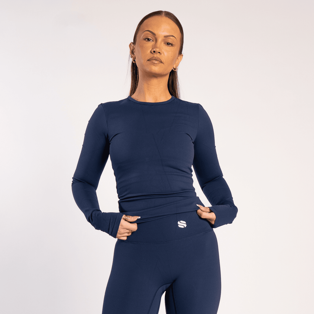 A person wears a long-sleeved navy blue athletic shirt and matching high-waisted leggings against a plain light gray background.