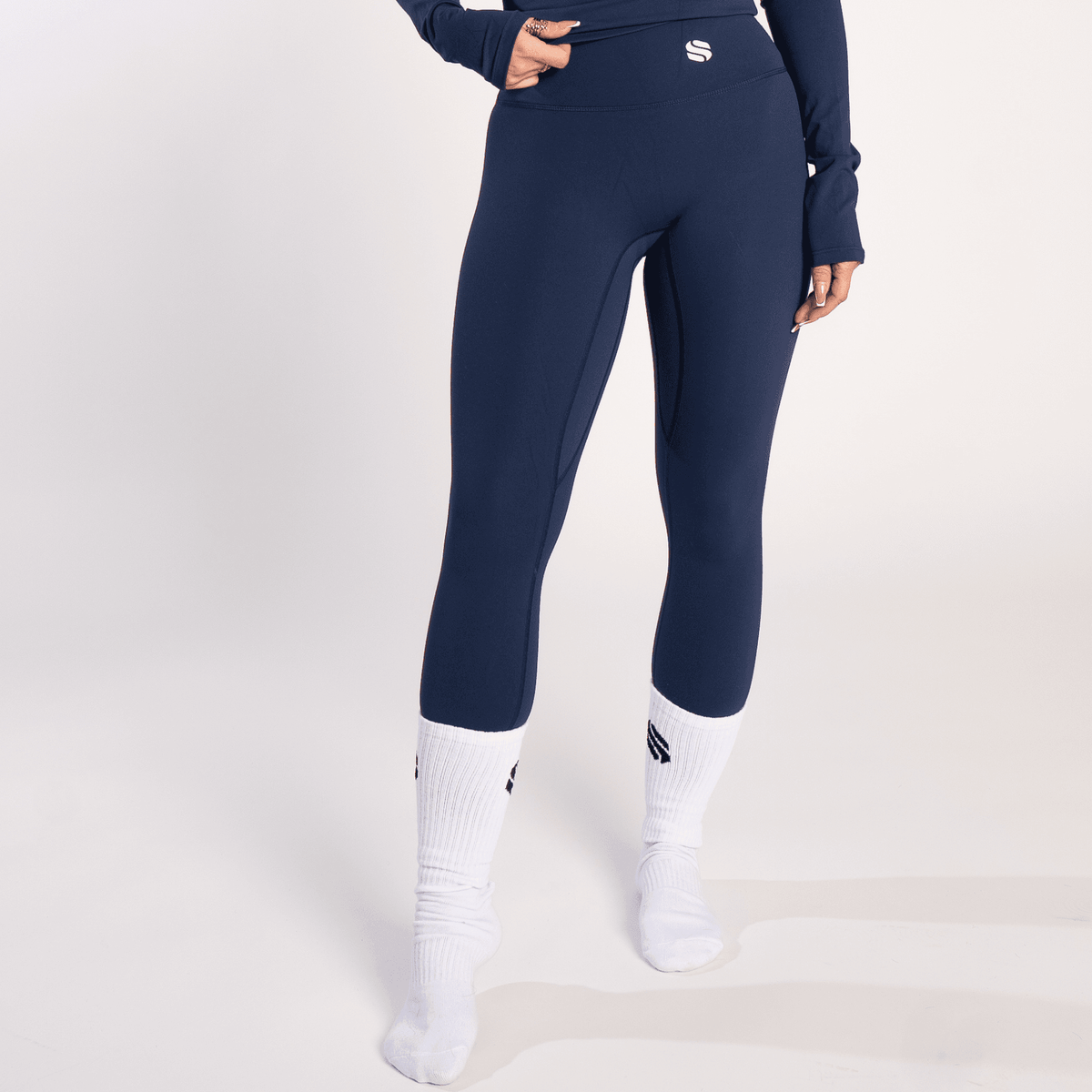 A person wears high-waisted navy blue leggings paired with white crew socks against a plain light grey background.