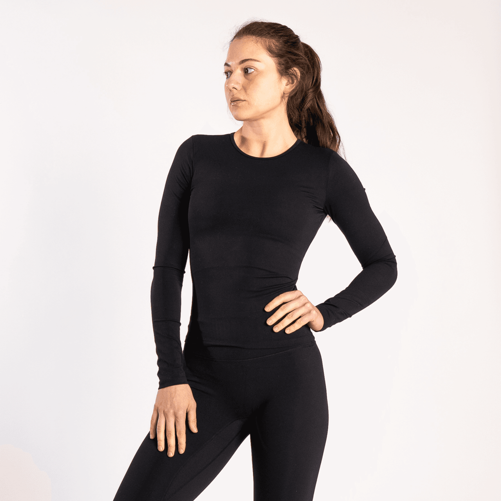 A person wears a black long-sleeved crew-neck top and matching black leggings while posing against a plain white background.