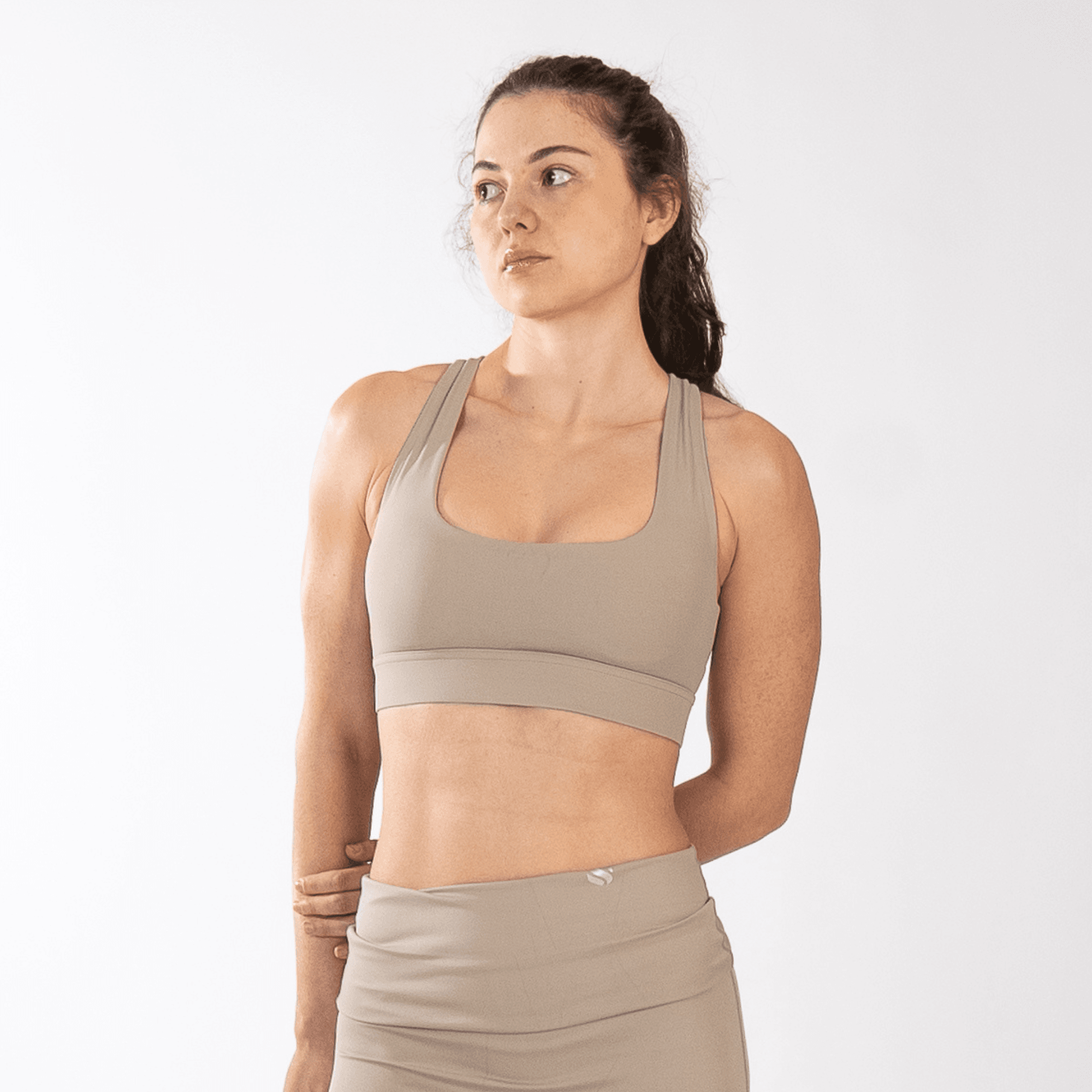 A woman wears a light beige athletic sports bra with a scoop neckline and a racerback strap design.