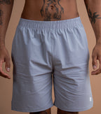 A close-up of a man wearing light gray athletic shorts, showing the waist, hips, and upper thighs. The man has visible tattoos on his torso and arms.