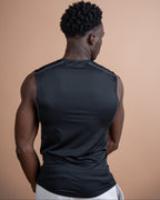 A man viewed from behind wearing a black sleeveless athletic compression shirt against a solid warm beige studio background.