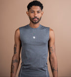A man wearing a sleeveless heather gray athletic shirt with a small white logo on the chest, standing against a solid tan background.