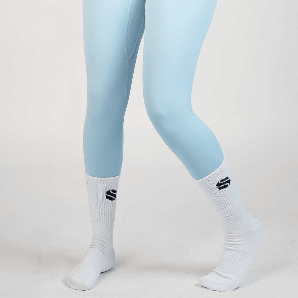 A pair of light blue leggings worn with white mid-calf ribbed socks featuring a black geometric logo on a plain white background.