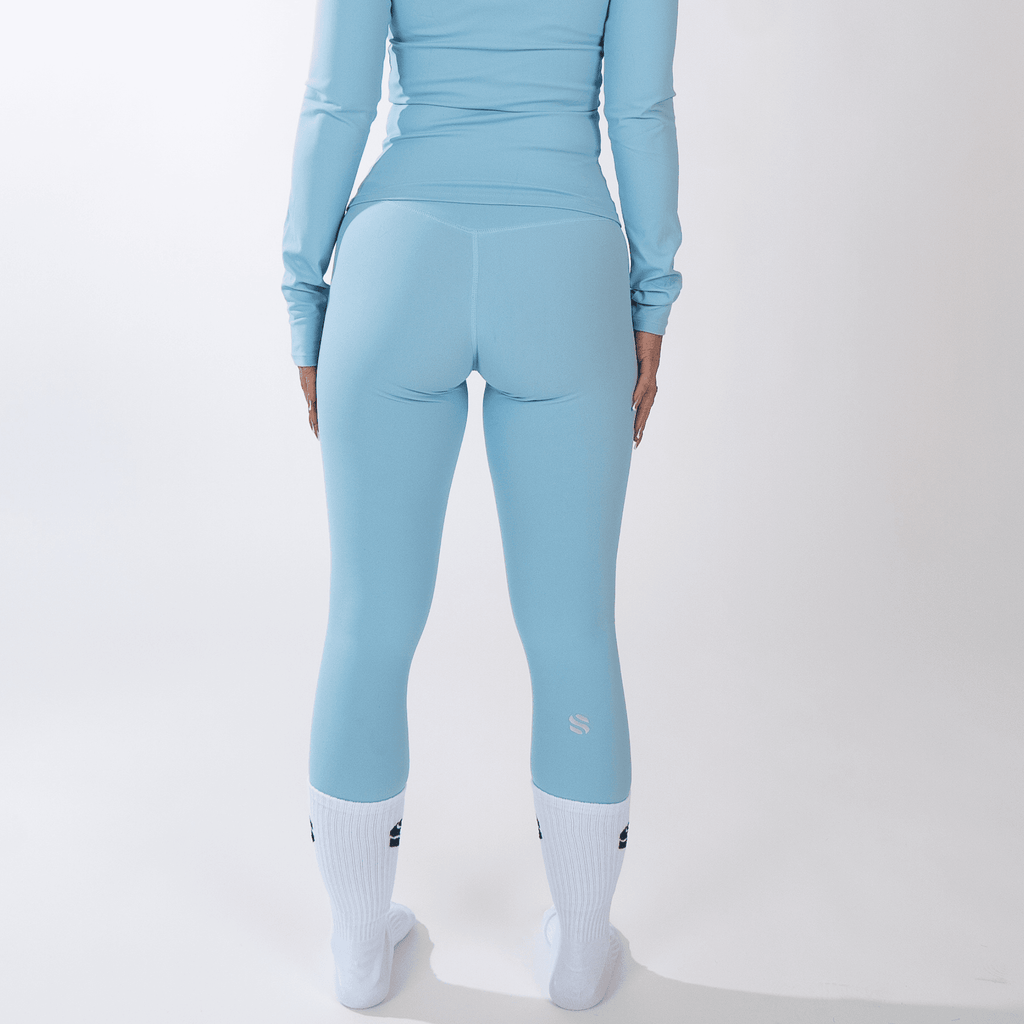 A person viewed from behind wearing light blue leggings and a matching long-sleeved top with white socks against a plain white background.