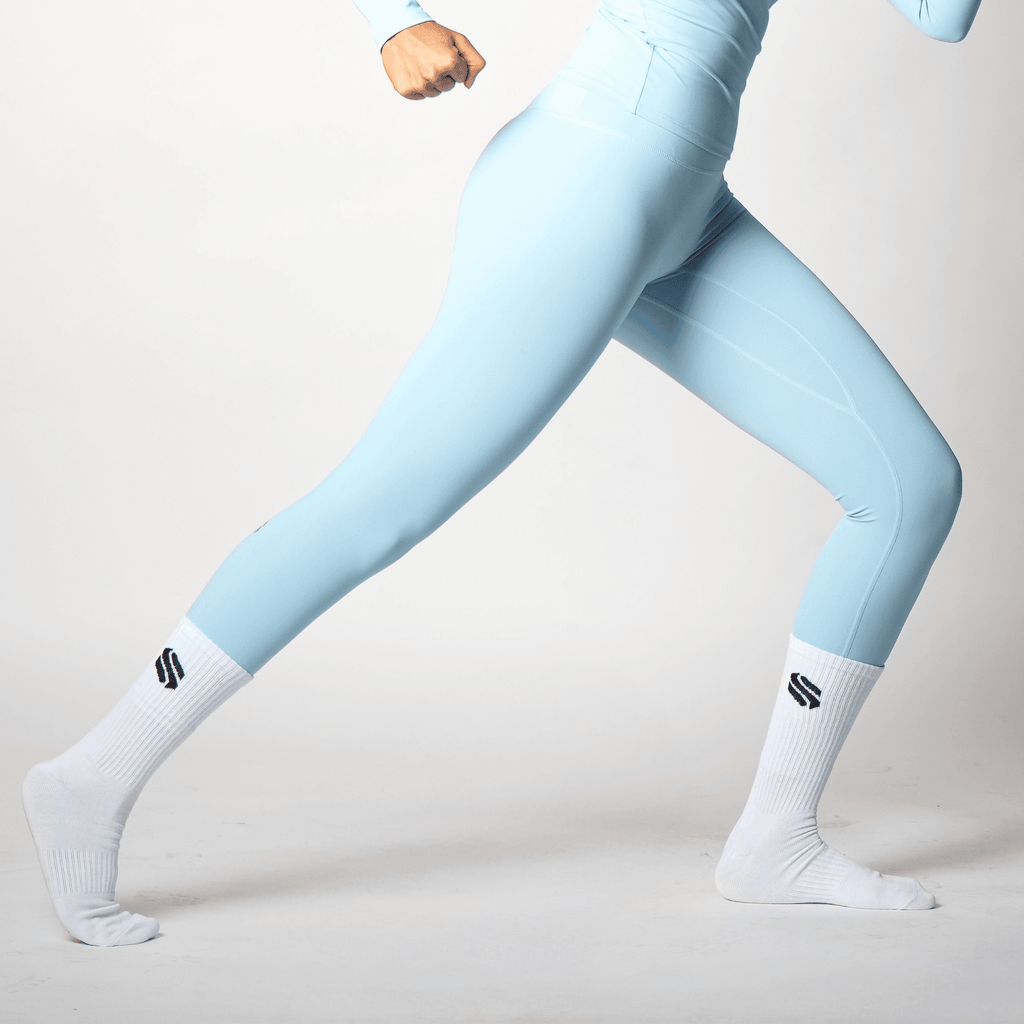 Light blue leggings worn by a person in a lunging position, paired with white athletic socks featuring a black logo on the side.