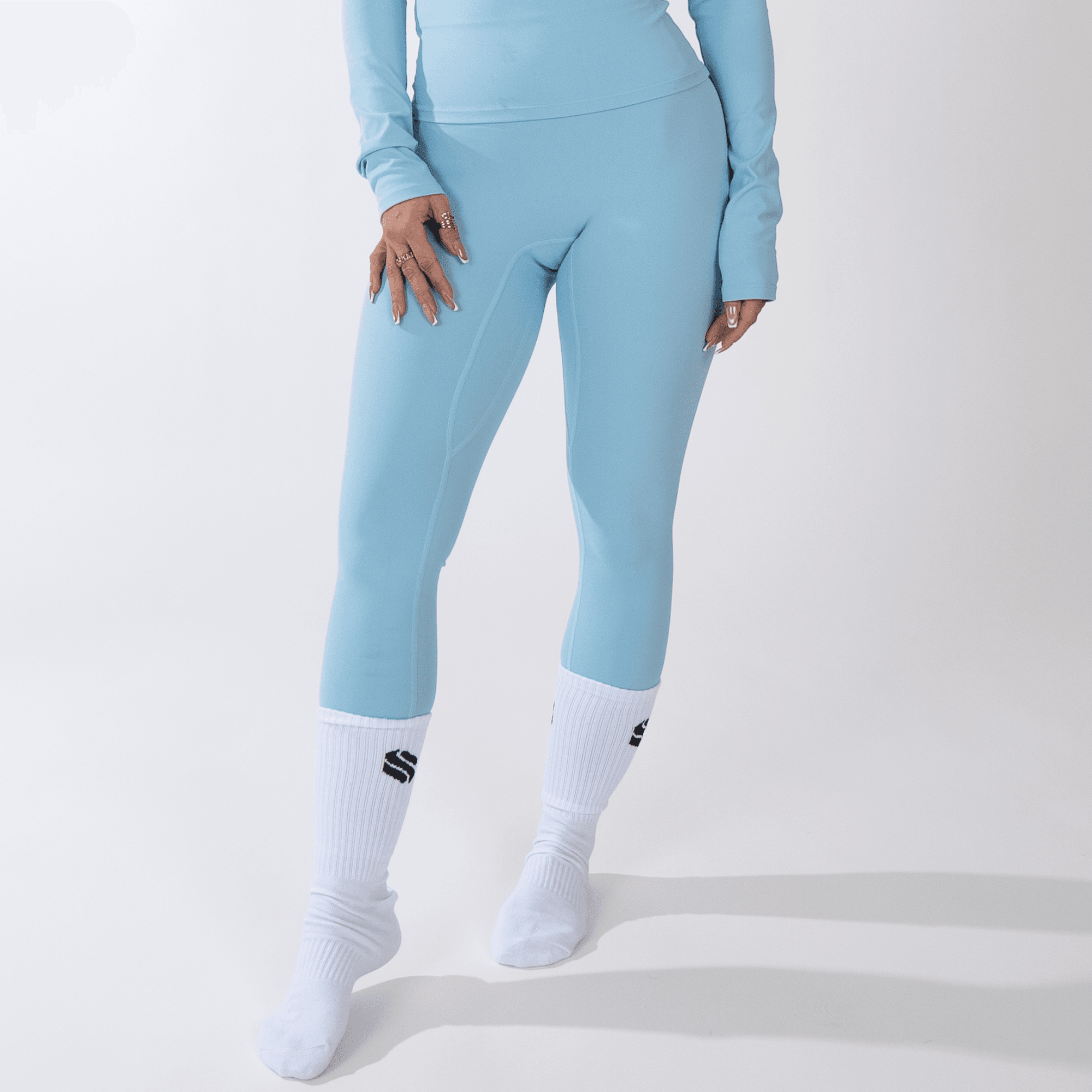 Light blue leggings worn with a matching long-sleeved top and white crew socks against a plain white background.