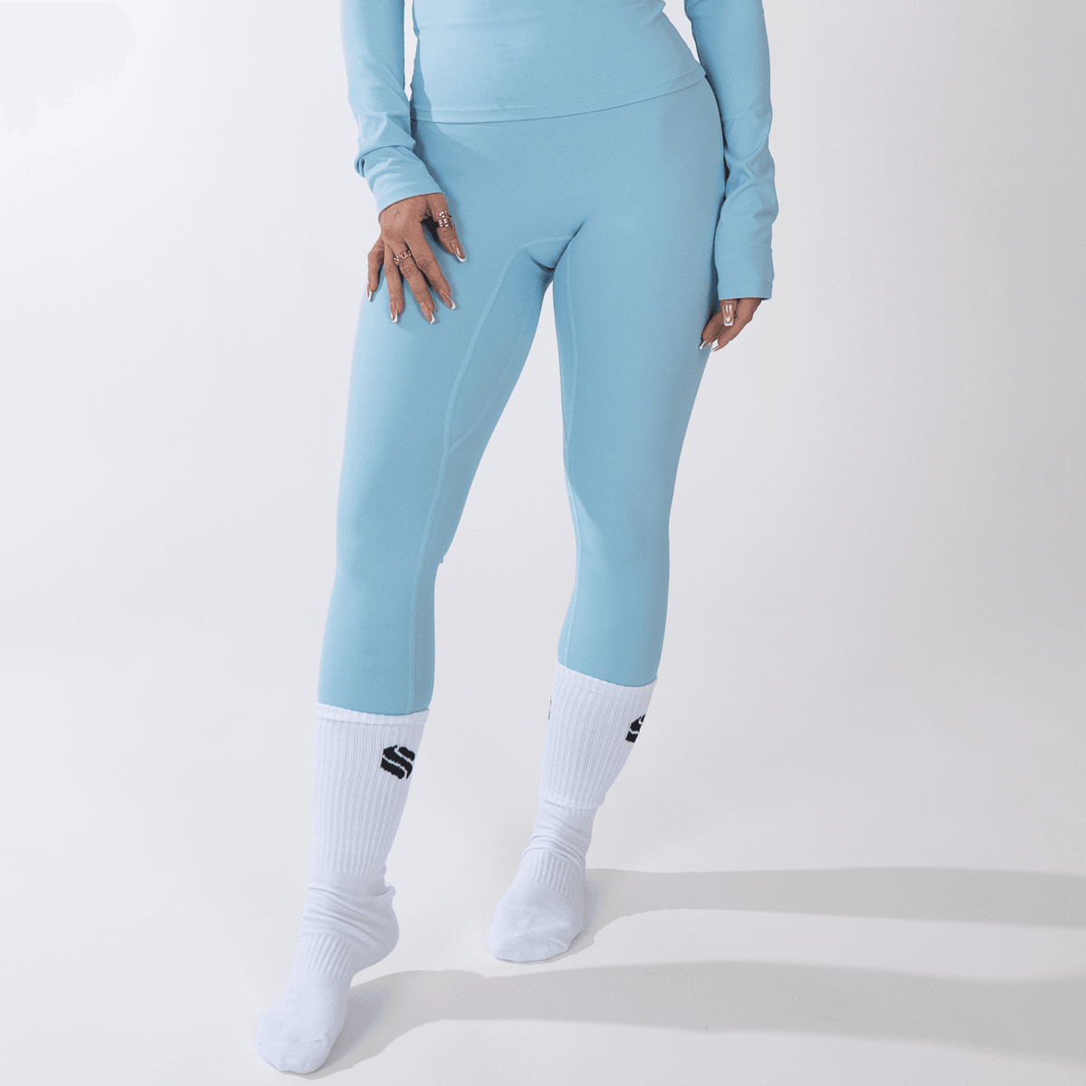 Light blue leggings worn with a matching long-sleeved top and white crew socks against a plain white background.