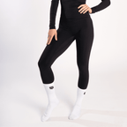 A person wears black leggings and a matching long-sleeved top with white mid-calf socks featuring a black logo.