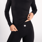 A person wears a black long-sleeved top tucked into matching high-waisted black leggings, featuring a small white logo on the waistband.