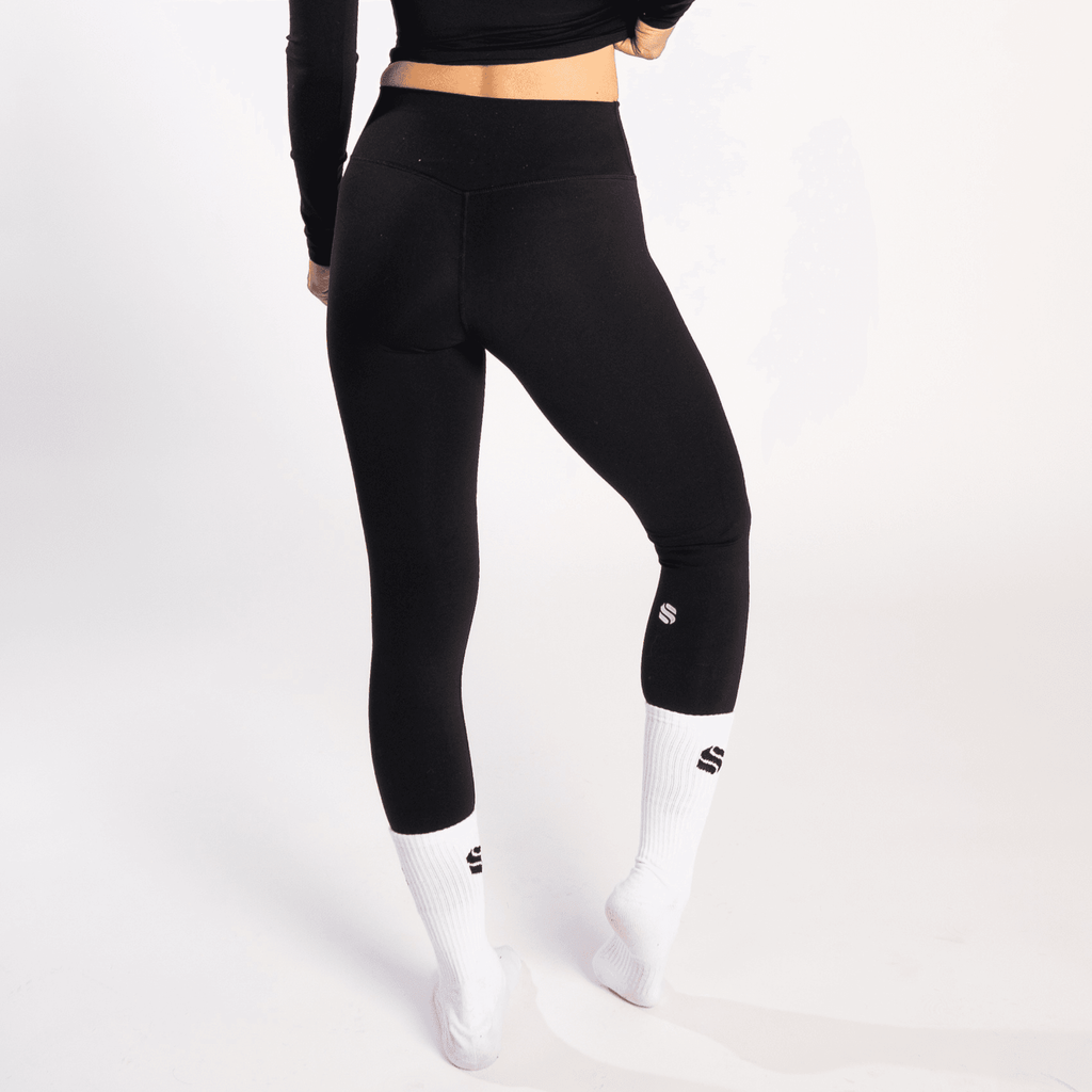 Black high-waisted leggings worn by a person with white athletic socks featuring small black logos on a plain white background.
