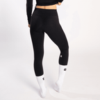 Black high-waisted leggings worn by a person with white athletic socks featuring small black logos on a plain white background.