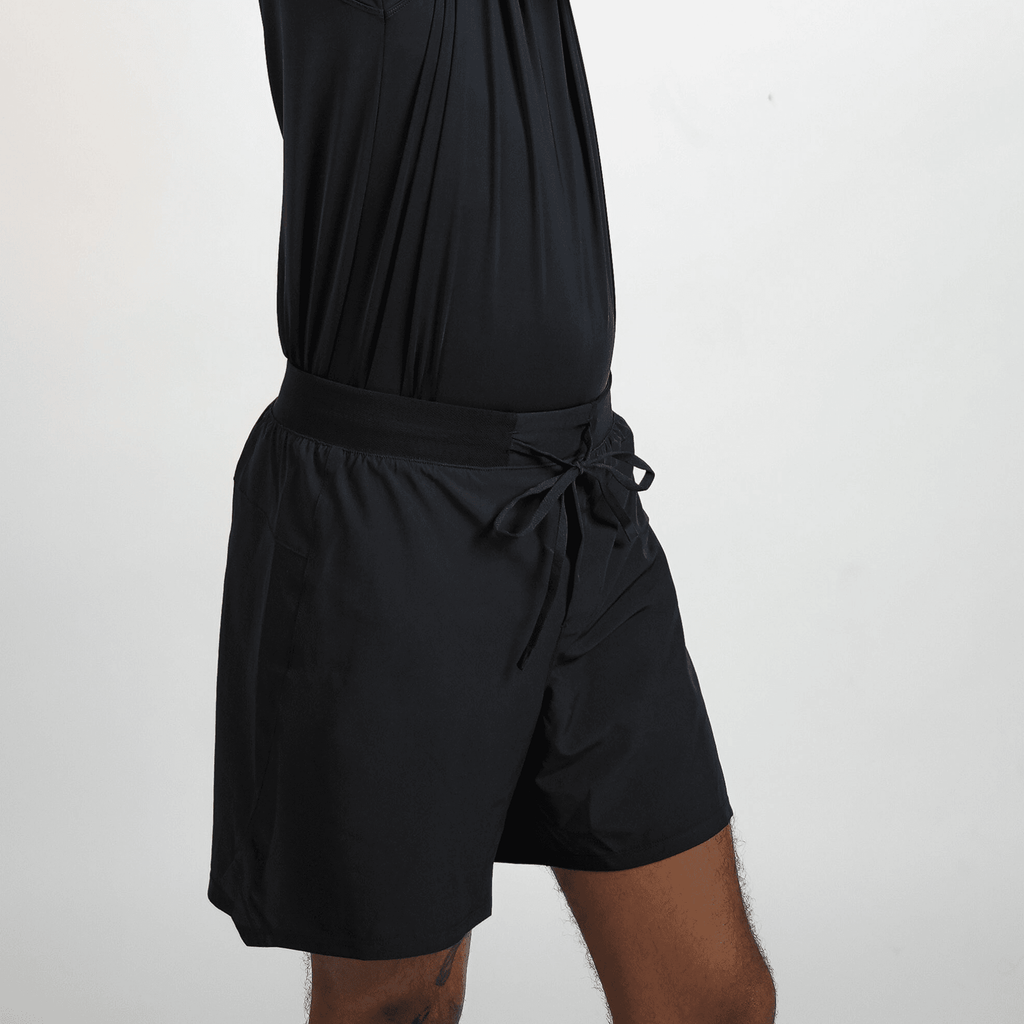 Black athletic shorts for men with a wide elastic waistband and a drawstring tie, shown from a side profile view against a plain light background.