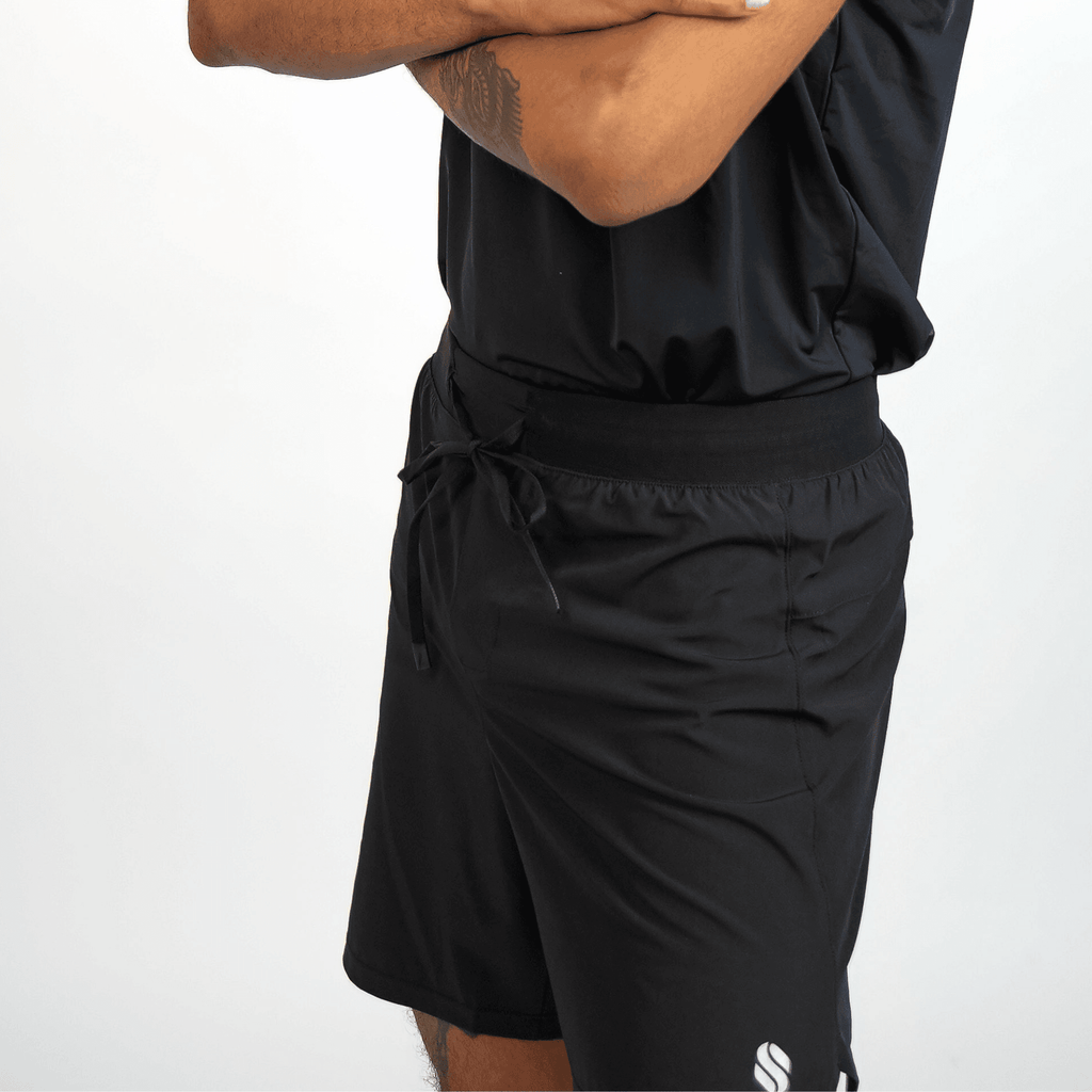 A man wearing plain black athletic shorts with an elastic drawstring waistband and a small white logo near the hem.