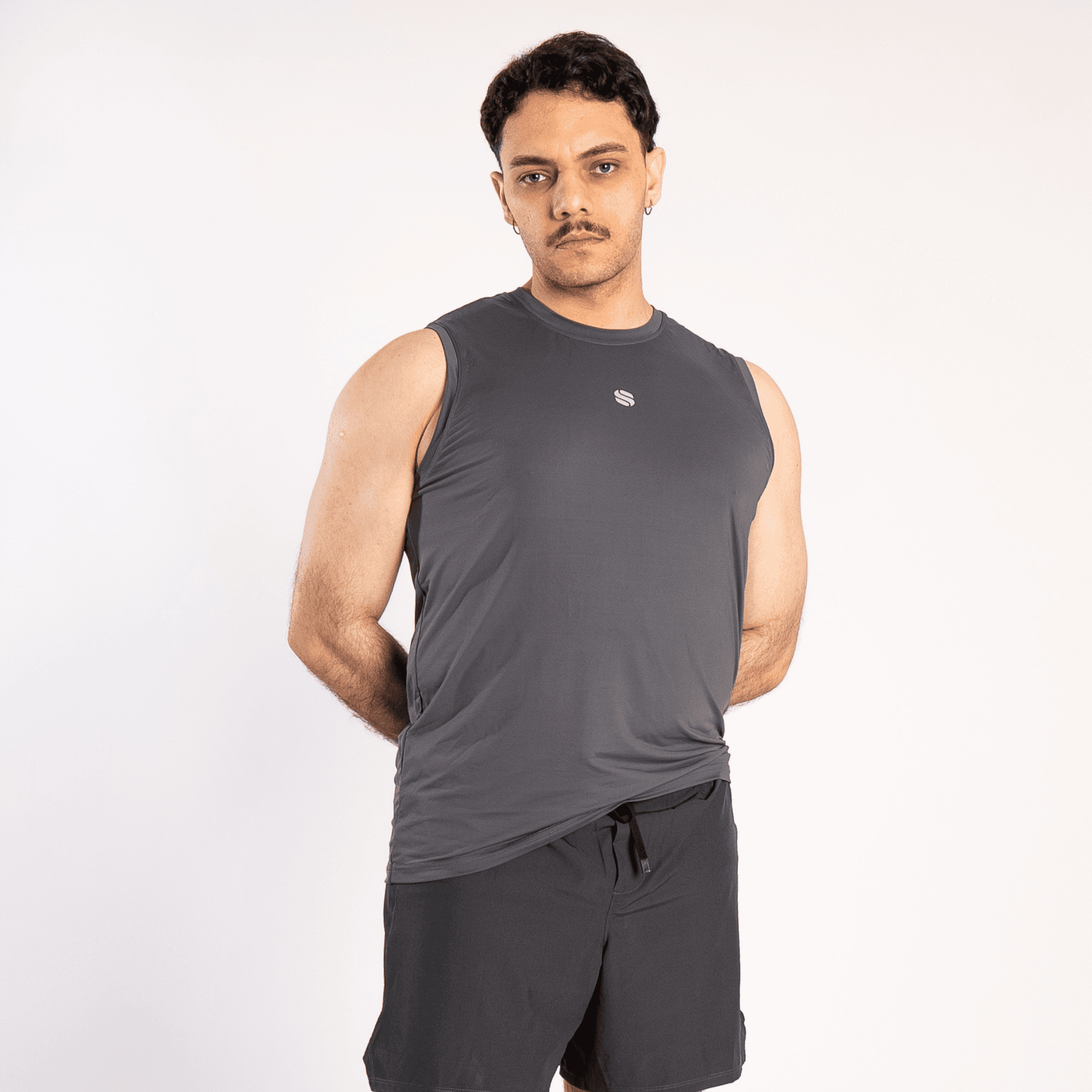 A man wearing a charcoal grey sleeveless crew neck tank top with a small white logo on the chest and matching black athletic shorts against a plain white background.