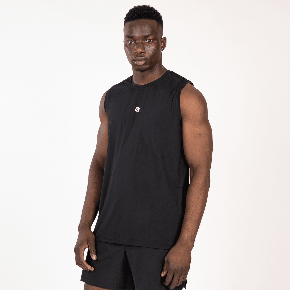 A man wearing a plain black sleeveless workout tank top and matching black athletic shorts stands against a white background.