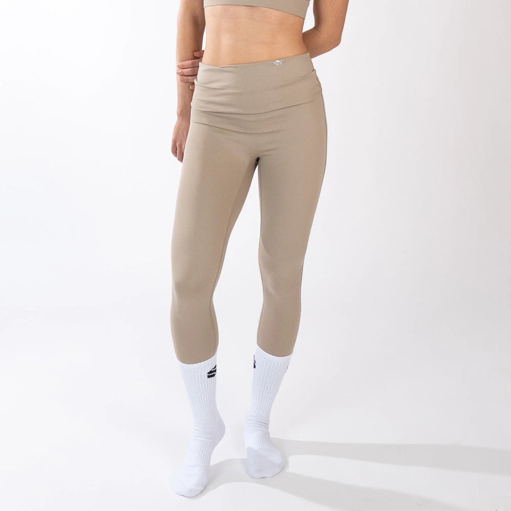 A person wearing tan, high-waisted, cropped leggings paired with white crew socks against a plain white background.