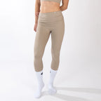 A person wearing tan, high-waisted, cropped leggings paired with white crew socks against a plain white background.