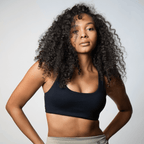 A black sports bra with a scoop neckline worn by a person with long curly hair against a plain grey background.